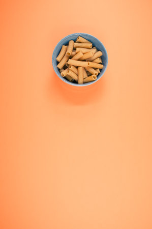 A top view of a little bowl with uncooked Rigatoni isolated on an orange background with free spaceの写真素材