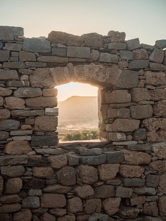 A vertical shot of a window on a stone wall with a sunrise backgroundの写真素材