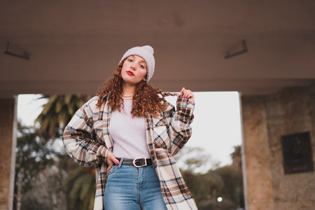 A stylish young female wearing a plaid jacket, white warm hat, jeans in the parkの写真素材