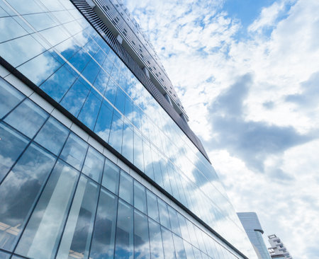 A low angle shot of the exterior of a modern building with the reflection of a blue cloudy skyの写真素材