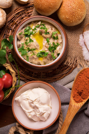 A top view of delicious mushroom soup and sour cream in clay bowls on a straw trivet in a kitchenの写真素材