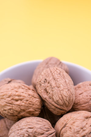 A vertical shot of whole walnuts in a white bowl isolated on a yellow backgroundの写真素材
