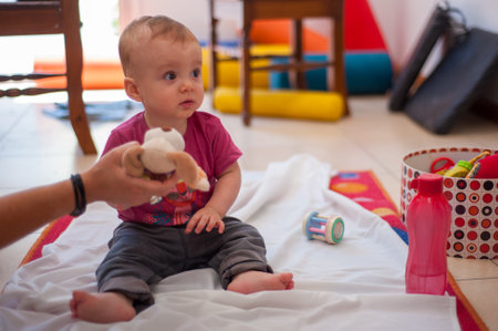 An adult person showing a stuffed animal toy to an adorable Argentine toddler on the floorの写真素材