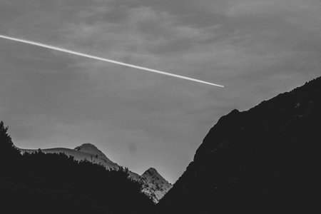 A grayscale shot of a plane track on the sky above the rocky mountains