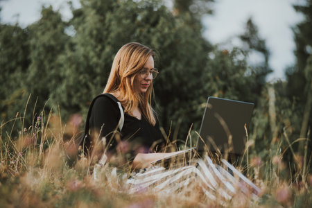 A woman sitting in the field working with her laptopの写真素材