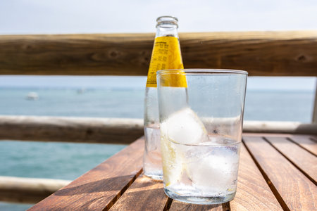 A bottle and glass of water with a slice of lemon and ice on a wooden tableの写真素材