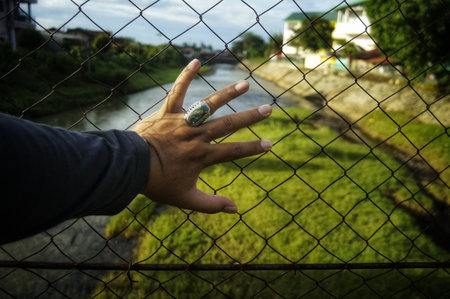 The mans hand on the metal fence with the blurred grassfield in the backgroundの写真素材