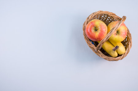 A top view of a basket with fresh tasty sweet bananas and apples on the blue surfaceの写真素材