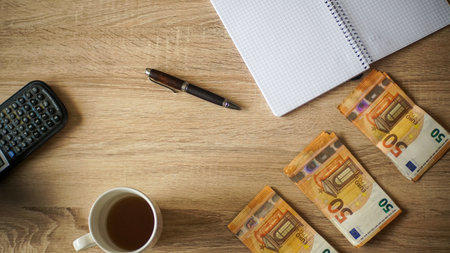 A top view of a cup of coffee a notebook and euros on the tableの写真素材