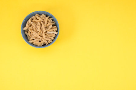 A top view of a bowl of cooked pasta on a yellow background with copy space on the rightの写真素材