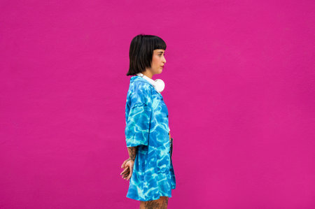 A side-view of a charismatic brunette young woman from Spain in a vibrant blue shirt in a pink...