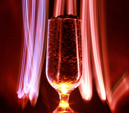 A long exposure shot of coffee beans in a transparent cup with led lights on a background