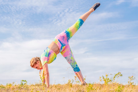 Beautiful girl gymnast in a bright tracksuit is engaged in sports outdoors. Performs muscle stretching exercises. Healthy lifestyle.の写真素材