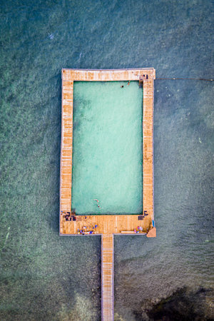 An aerial view of a rectangular pool in the middle of the sea with people having a restの写真素材