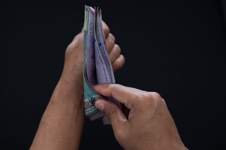 A closeup of man's hands counting Malaysian banknotes on a black background - finances and payment...
