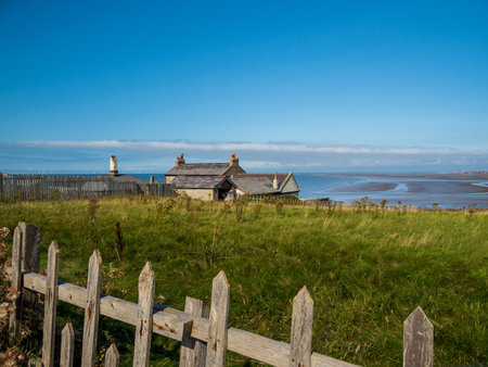 a closeup shot of wooden fences, building background surrounded by grass, trees in hilbre islandの写真素材