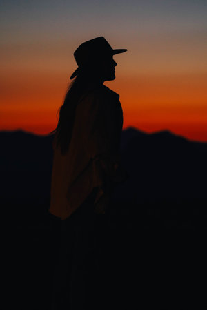 A vertical shot of a silhouette of a female during the sunset with a mountain in the backgroundの写真素材