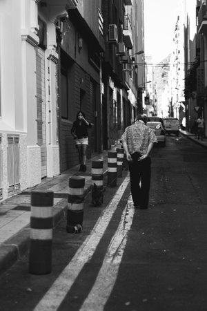 A grayscale vertical shot of a narrow street with people walkingの写真素材