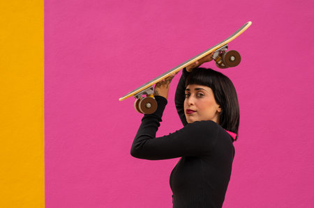 A beautiful young female posing with a skateboard on pink and yellow backgroundの写真素材