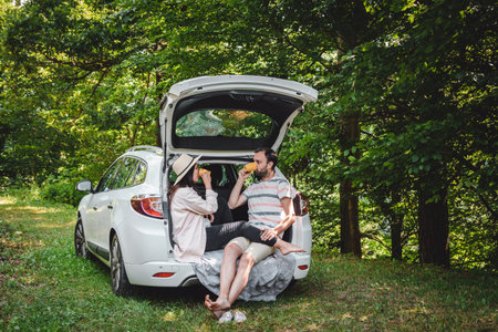 Young couple sitting in boot of car parked in forest, drinking coffee.の写真素材