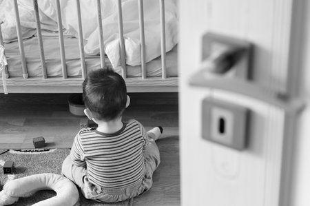 A grayscale shot of a toddler boy playing on the floorの写真素材