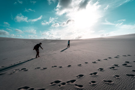 A beautiful view of people walking in a desert with sand dunes in the sunlightの写真素材