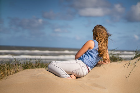 A back view of a young female watching the seascape from the sandy beachの写真素材