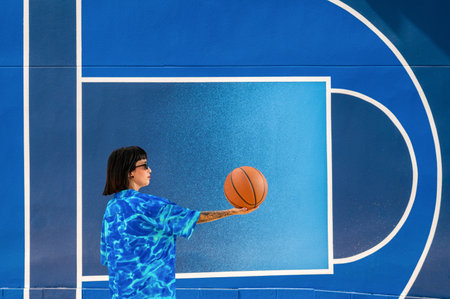 A side shot of a Caucasian girl from Spain in sunglasses holding a basketball ball on blue backgroundの写真素材