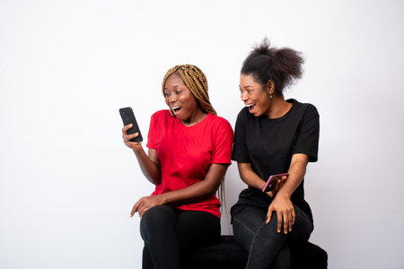 A pair of young African female friends happily shocked at a phone isolated on a white backgroundの写真素材