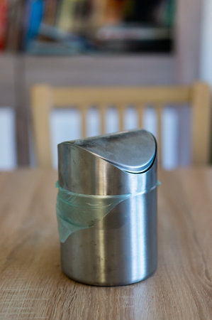 A vertical shot of a small metal waste container on a wooden tableの写真素材