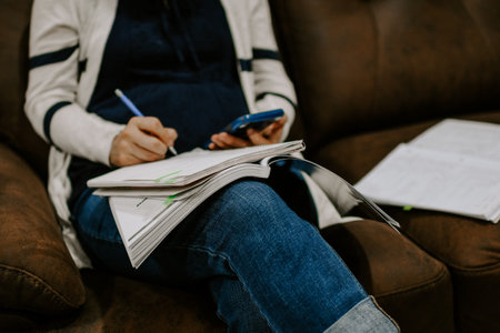 A closeup shot of a female taking notes while reading off a smartphoneの写真素材