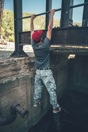 A young man in a red cap doing pull-up exercises on a bar of a metallic structurの写真素材