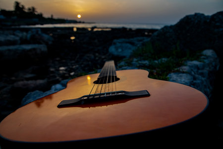 A closeup shot of a brown wooden guitar lying on the rocks at the seaside during late sunset in Havana, Cubaの写真素材