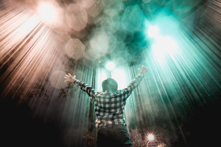 A young boy with raised hands looking to the illuminated light raysの写真素材