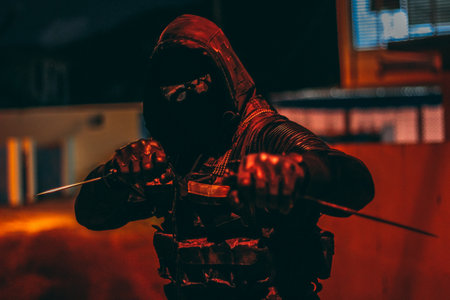 A male wearing black clothes, gloves and glasses posing with two knives in his handsの写真素材