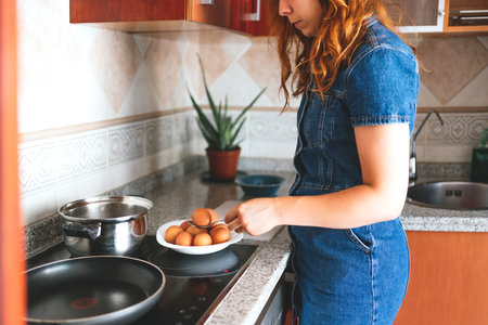A young Caucasian housewife taking out the boiled eggs from a stainless steel pot in the kitchenの写真素材