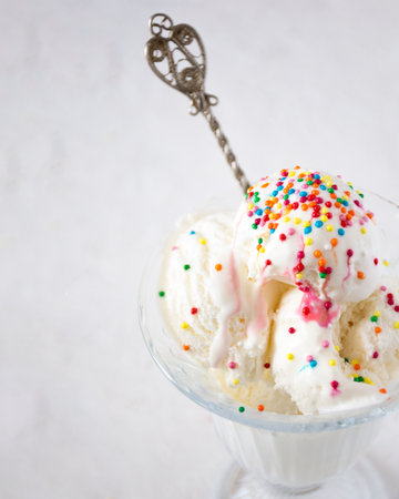 We see scoops of vanilla ice cream with colorful sprinkles on it, melting.の写真素材