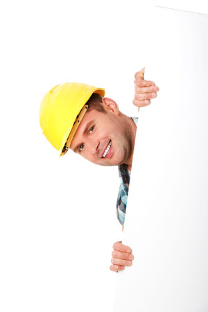 A young happy engineer in a helmet hiding behind a blank posterの写真素材