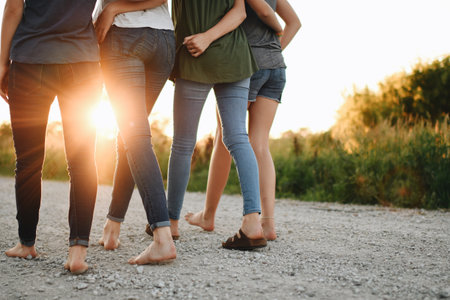 A back view of a group of female friends hugging and walking outdoors on a sunny dayの写真素材