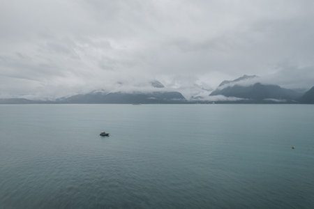 A fishing boat sailing in a lake surrounded by hills and mountains on a foggy morning in Alaskaの写真素材