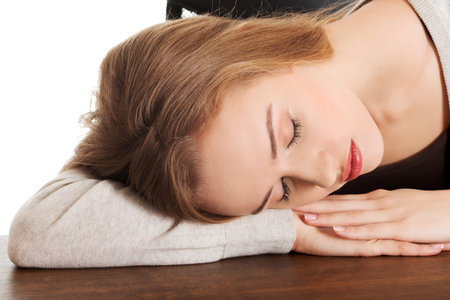 A young tired Caucasian female sleeping on a tableの写真素材