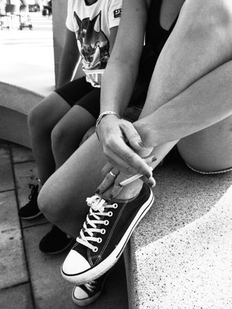 A vertical grayscale shot of a woman's leg as she holds it with a cigarette in her handの写真素材