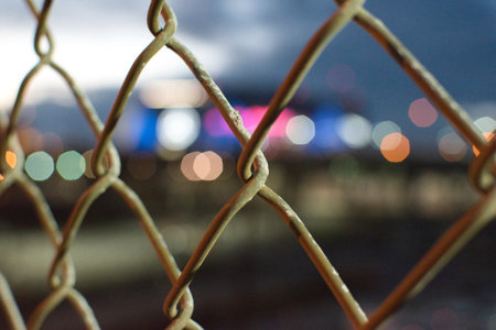 A closeup shot of a wire mesh fence on the background of bokeh lights of the cityの写真素材