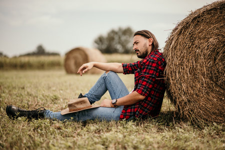 A young handsome Serbian male in a flannel shirt and ripped jeans sitting leaned on a haystackの写真素材