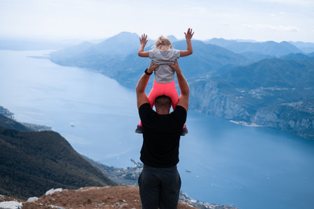 A father holding his daughter over his head and looking at the Garda lake in North Italyの写真素材