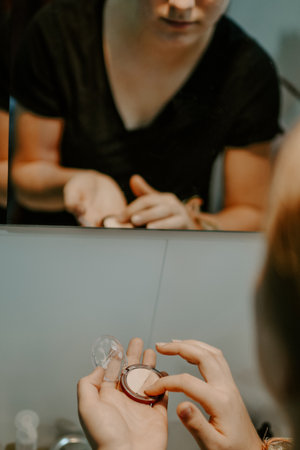 A vertical closeup shot of a female putting on blush in a bathroom mirrorの写真素材