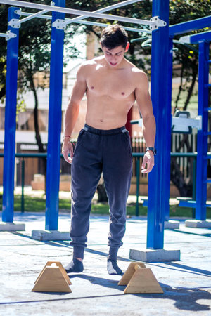 A vertical shot of a muscular Hispanic bodybuilder working out at a street gym
