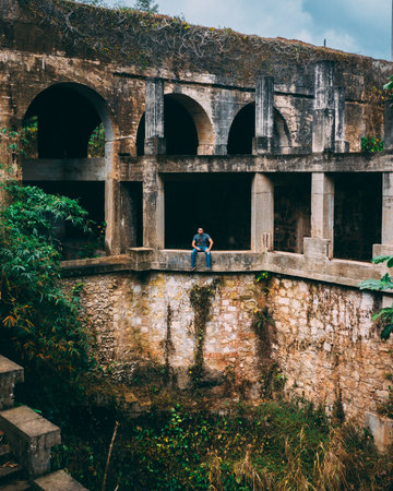 A vertical shot of a person sitting on the wall of an old abandoned fortressの写真素材