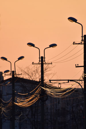 A vertical shot of electricity cables and old street lamps during sunsetの写真素材