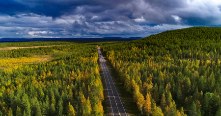 Aerial view following a white RV car driving on a fall road, between colorful autumn forest, sarkijarvi lake and fjeld mountains, Lapland, Finlandの写真素材